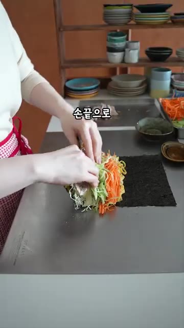 속 재료를 감싸듯이 단단하게 말고 김 끝에 물을 묻혀 고정한다. — 밥 빼야 더 맛있는 김밥