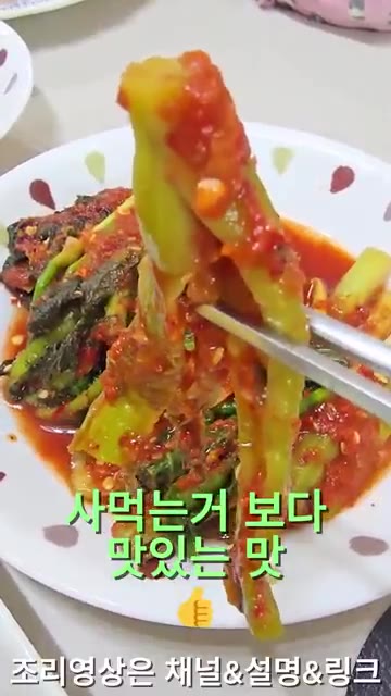 여수 갓김치를 집게로 들어 보여주며 맛을 강조한다. — 26년 가을 집밥일기: 청양 데리야끼 닭다리살과 다양한 김치, 장조림 등