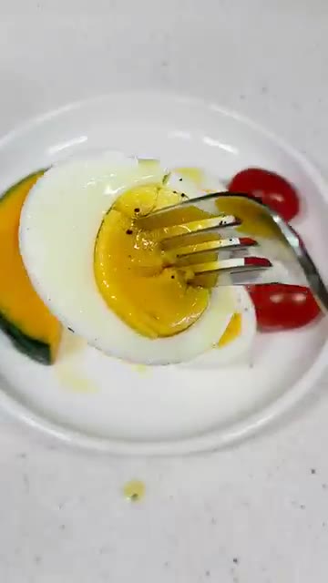 포크로 달걀을 찍어 맛있게 먹는다. — 천연 위고비 식단: 올리브 오일, 단호박, 토마토, 달걀을 곁들인 건강한 아침 식단